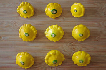 Close-up view directly from above of an arrangement of nine organic yellow sunburst squash vegetables on a bamboo cutting board