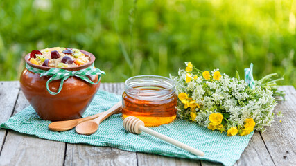 Homemade Breakfast in nature from oatmeal porridge with pieces of fruit and berries and young honey.