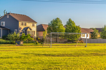 Soccer goal on vast green grassy field in front of houses viewed on a sunny day