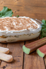 selbstgemachtes Tiramisu mit Rhabarber, Creme, Sahne, Zimt, Löffelbiscuit und Mascarpone auf einem Tisch aus Holz