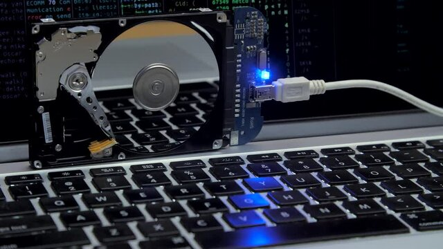 Hard drive lies on the laptop keyboard, flashes and disk spins. Work of hacked hard drive inside. Cybersecurity. Internal Structure of HDD. Lines of code and data flash on background