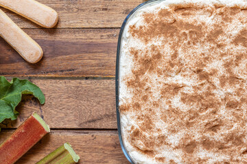 selbstgemachtes Tiramisu mit Rhabarber, Creme, Sahne, Zimt, Löffelbiscuit und Mascarpone auf einem Tisch aus Holz