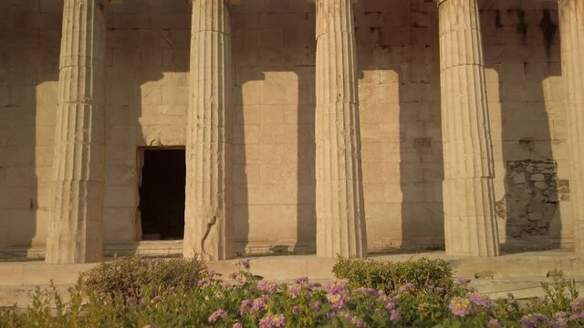 View of the Temple of Hephaestus, the best well-preserved Greek temple, on the ancient Agora of Athens, Greece. Tilt up shot with nautral light and flowers in the foreground.