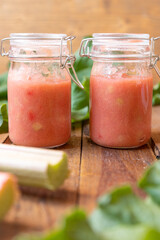 selbstgemachter gekochter rosa roter Rhabarbermus mit Stücken im Glas auf einem braunen Tisch aus Holz