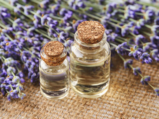 Obraz na płótnie Canvas Two glass bottles of lavender essential oil and fresh fragrant lavender on a jute sackcloth background. Spa, beauty, skin care and cosmetology concept.