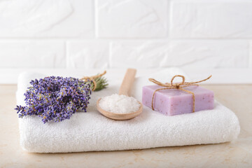 Obraz na płótnie Canvas Fresh fragrant lavender, cosmetic bath salt in a wood spoon and lavender soap on a white terry towel in a bathroom. Home made spa, skincare and cosmetology concept.