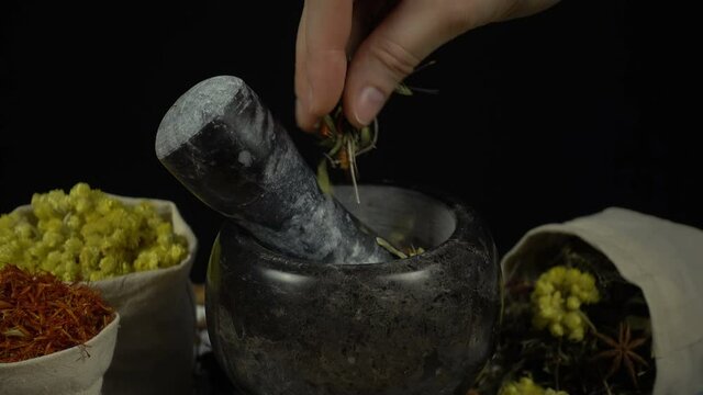 Woman's hand puts herbs and flowers into the granite mortar with pestle. Healthy and organic food, herb medicine, natural care, aromatherapy and organic cosmetics concept.