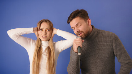 Young woman can't take the noise of her boyfriend singing. Closing the ears with hands and making...