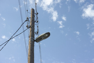 An old electric wooden pole with a lamp and electricity cables hanging on. Natural light.