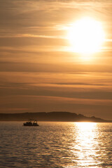 Naklejka na ściany i meble Fishing boat returning home at sunset.