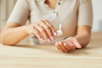 Close up of unrecognizable mixed-race woman using gel sanitizer to clean hands while sitting at wooden table, copy space