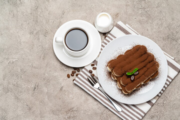 Classic tiramisu dessert on ceramic plate, milk or cream and cup of coffee on concrete background