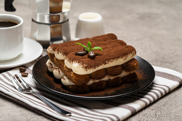 Classic tiramisu dessert on ceramic plate, milk or cream and cup of coffee on concrete background