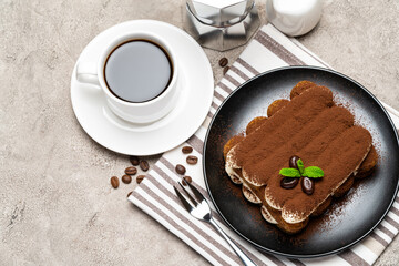Classic tiramisu dessert on ceramic plate, milk or cream and cup of coffee on concrete background