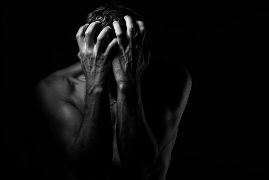 Man covers his face with his hands. Regret or fear. On a dark background. Black and white photography.
