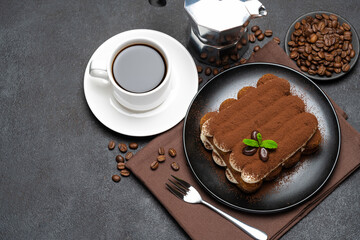 Classic tiramisu dessert on ceramic plate, milk or cream and cup of coffee on concrete background