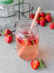 Strawberry lemonade with rosemary and ice in mason jar on a gray concrete table. Seasonal food concept. Summer harvest time