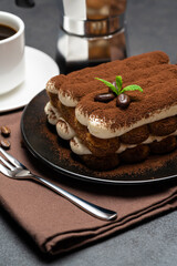 Classic tiramisu dessert on ceramic plate, milk or cream and cup of coffee on concrete background
