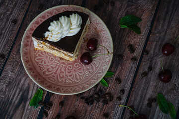 Obraz na płótnie Canvas Piece of cake with cream on plate. Chocolate cake on wooden background with coffee beans and mint leaves. Delicious slice of layered tart on plate. Baking and decorating chocolate cake.