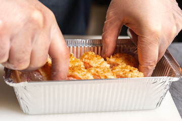 A sushi chef puts a tempura fried roll in an aluminum delivery box