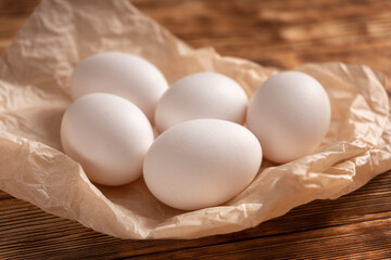 Rustic chicken eggs on parchment paper on a wooden plank table.