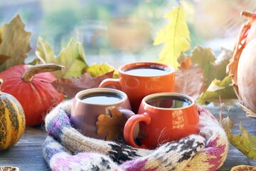 Three cups of coffee, pumpkins, leaves, a woolen scarf on a window background, the concept of home comfort, family, Thanksgiving, autumn season