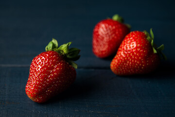 A few ripe red strawberries on dark blue wooden background. Space for text.