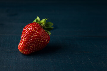 Ripe red strawberry on the dark blue wooden background. Space for text.