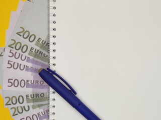 against the background of 100 200 and 500 Euro notes. close-up, pen on a Notepad with a copy space,