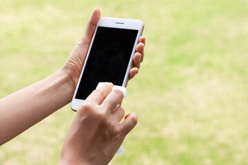 Thai woman wipes her hands with an alcohol towel washing mobile smartphone. Coronavirus prevention for hand hygiene corona virus protection. COVID-19 prevention sanitizing inside.