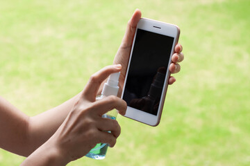 Thai woman wipes her hands with an alcohol based mobile smartphone washing spray. Coronavirus prevention for hand hygiene corona virus protection. COVID-19 prevention sanitizing inside.