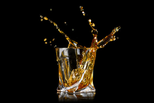 Splashing of whiskey out of glass isolated on black