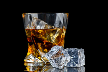 Glass of whiskey with cube ice on black background