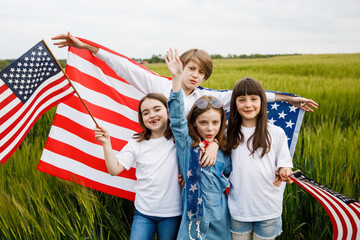 Four cheerful children stand in a field with an American flag in their hands