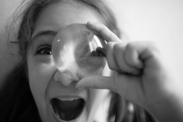Little girl looks with one eye through the lens on a light background