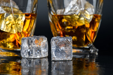 Glass of whiskey with cube ice on black background