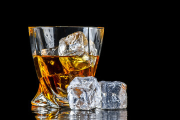 Glass of whiskey with cube ice on black background