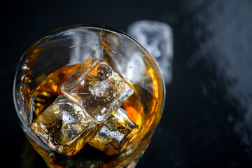 Glass of whiskey with cube ice on black background