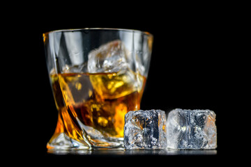 Glass of whiskey with cube ice on black background