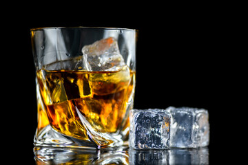 Glass of whiskey with cube ice on black background