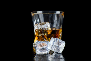 Glass of whiskey with cube ice on black background