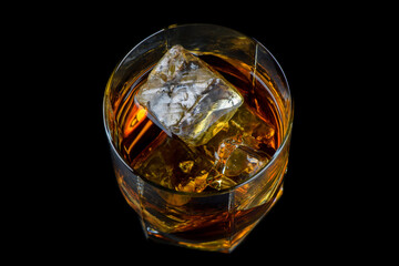 Glass of whiskey with cube ice on black background