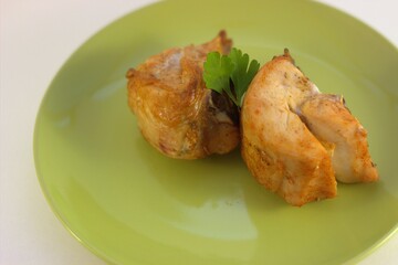 Two delicious pieces of grilled chicken breast lie on a green plate. Side view