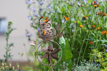 Eulen Windspiel ruht im Blumenmeer. Bronze farbenes Windspiel steht zwischen grünen Stängeln von...