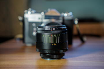 Altes manuelles Retro Objektiv aus Metall steht vor einer analogen Kamera mit Film. Schwarzes...