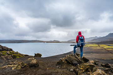 Obraz premium Man hiking in Iceland standing on the peak of rocks with backpack looking at the stunning view near the Kleifarvatn lake in Reykjanesfólkvangur nature reserve park
