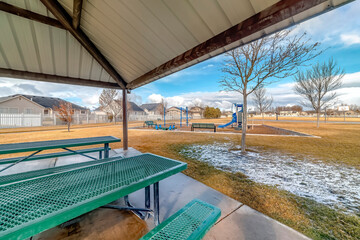 Green metal tables and benches inside a pavilion with melted snow on a sunny day