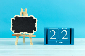 wooden calendar with the date of June 22 and an easel on a blue background, place for text