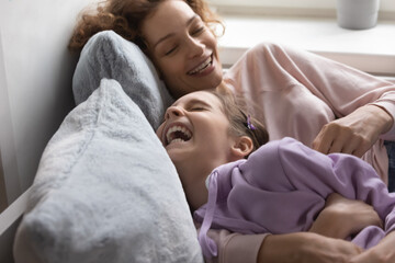 Loving young Caucasian mother have fun play with smiling teenage daughter relaxing in bed together,...