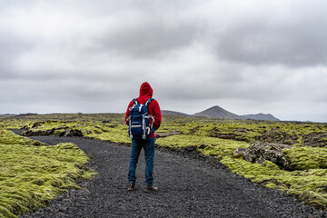 Man hiking in Iceland with backpack looking at the beautiful view of mountains surrounded by volcanic rocks and green moss near the Blue Lagoon in Reykjanes Peninsula
